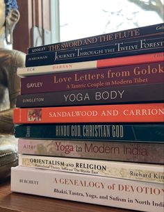 a stack of books sitting on top of a wooden table next to a vase and chair