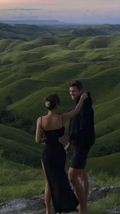 a man and woman standing on top of a lush green hillside