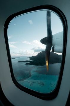 an airplane wing is seen through the window as it flies over some water and land