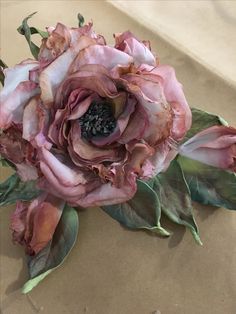 a large pink flower sitting on top of a piece of paper with leaves around it