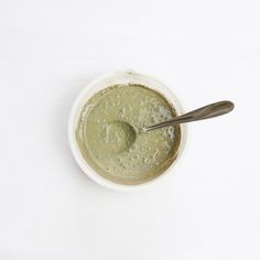 a white bowl filled with green liquid and a spoon