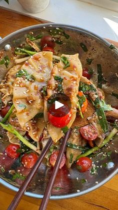 a pan filled with pasta and veggies on top of a wooden table next to chopsticks