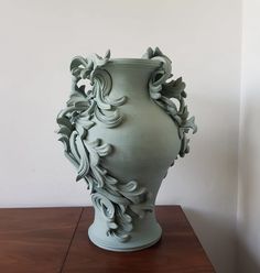 a large green vase sitting on top of a wooden table next to a white wall