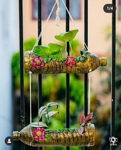 two wine bottles are hanging from a metal fence with plants growing out of the top