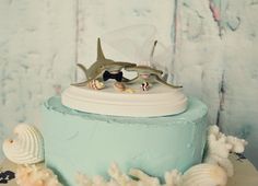 there is a blue cake with a shark on top and sea shells around the edges