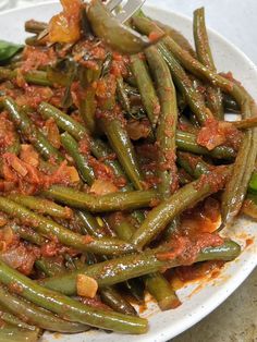 a white plate topped with green beans covered in sauce and seasoning next to a fork