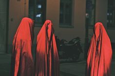 three people in red cloaks standing on the street