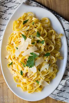 a white plate topped with pasta and parsley on top of a wooden table next to silverware