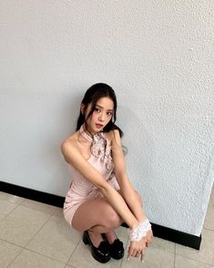 a young woman sitting on the floor with her legs crossed, wearing black shoes and a pink dress