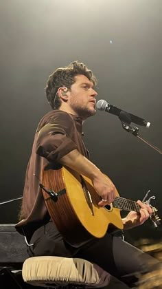 a man sitting in front of a microphone while holding a guitar and singing into a microphone