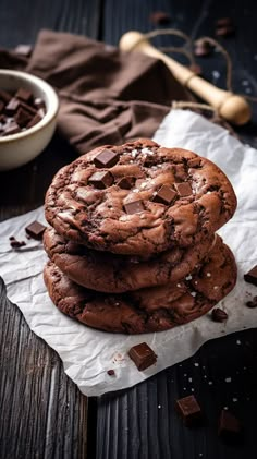 three chocolate cookies stacked on top of each other next to a bowl of chocolate chips