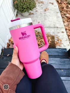 a person sitting on a bench holding a pink coffee cup with the name stanley in it