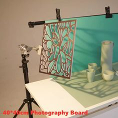 a camera and some cups are on a table next to a photo board that has been placed on a tripod