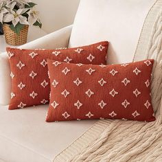 two red pillows sitting on top of a white couch next to a potted plant