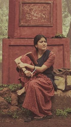 a woman sitting on top of a pile of dirt next to a red structure with writing on it