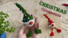 two small crocheted christmas ornaments are being held by someone's hand in front of a sign