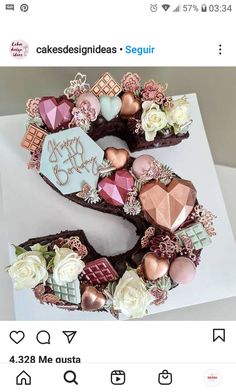 a chocolate cake decorated with pink flowers and gold decorations on top of a white table