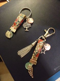 two keychains with charms attached to them on a black counter top next to a computer keyboard