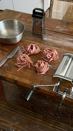 some pink pasta is on a wooden table with a metal bowl and spatula next to it