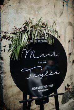 a black sign with greenery on it sitting in front of a wall that reads, married and taylor