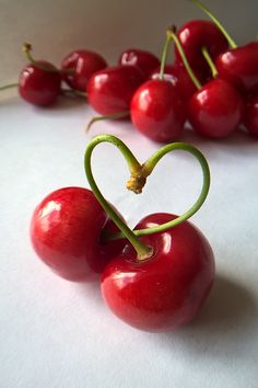 cherries are arranged in the shape of a heart on a white surface with green stems