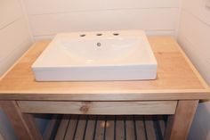 a white square sink sitting on top of a wooden counter in a bathroom next to a wall