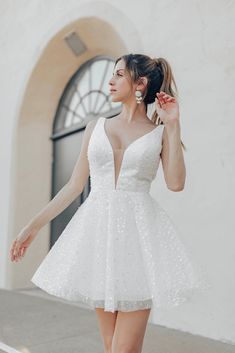 a woman in a short white dress is walking down the street with her hand on her hip