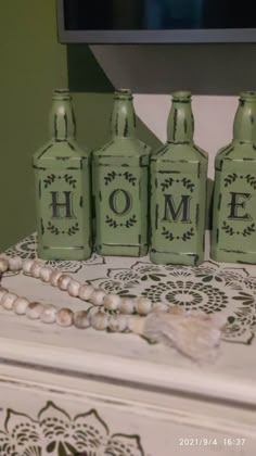 four green glass bottles sitting on top of a table next to a white beaded necklace