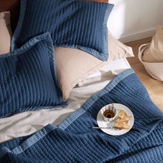 a plate of food on a bed with blue covers and pillows, next to a cup of coffee