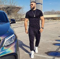 a man standing next to a car in a parking lot with his hand on his hip