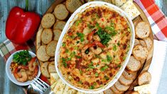 a platter filled with shrimp dip surrounded by crackers and vegetables on a checkered table cloth