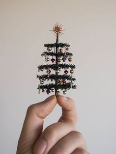 a hand holding a tiny christmas tree with ornaments on it's top and bottom