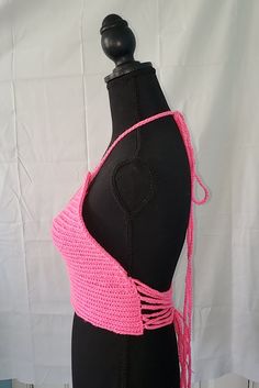 This crochet top is cotton candy pink in color. The strings tie around the neck as a halter top and interlace in the back. The adjustable ties can make the top fit looser if needed. If there is too much room around the waist, the ties may be tied more tightly. This yarn is stretchy and the lace-up back means it can fit various sizes. This particular top is recommended for sizes medium-large. This top does not have supportive cups or wiring built in. Strappy Tie Back Tops For Beach, Fitted Pink Strappy Halter Top, Strappy Summer Crop Top For Beach, Cross-tied Halter Top For Beach, Pink Sleeveless Crop Top For Beach, Pink Triangle Halter Top With Tie Back, Pink Triangle Top Crop Top For Vacation, Pink Crochet Crop Top For Vacation, Strappy Halter Top For Summer Festivals