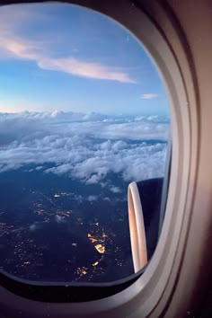 an airplane window looking out at the clouds and city lights in the distance as seen from inside