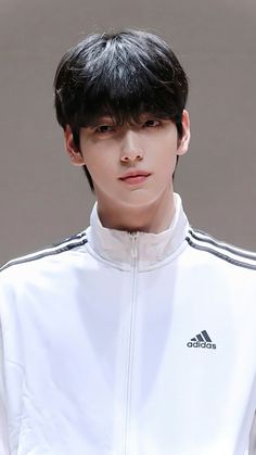 a man with black hair wearing a white adidas jacket and looking at the camera