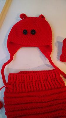 a crocheted red hat and diaper on a white surface with knitting needles