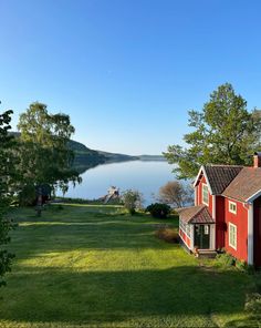 a red house sitting on top of a lush green field next to a body of water