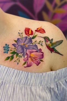 a woman's shoulder with colorful flowers and hummingbirds on her left side tattoo