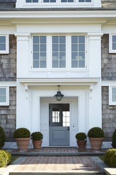 the front door of a large house with potted plants on each side and windows above it