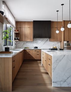 a kitchen with marble counter tops and wooden cabinets, along with hanging lights above the sink