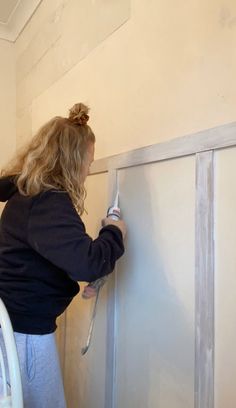 a woman is painting the wall with white paint