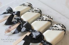 four pops decorated with black and white bows on wooden skewers, sitting on a marble surface