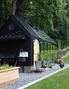 a small black shed sitting in the middle of a lush green yard with potted plants