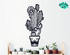 a metal cactus wall hanging on the side of a white wall next to potted plants