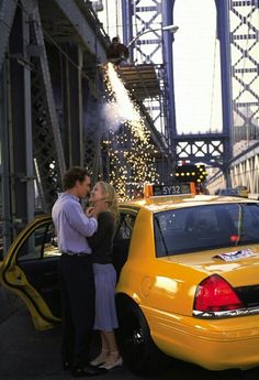 a man and woman standing in front of a taxi cab on the side of a bridge