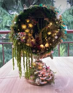 an arrangement of flowers and plants in a vase on a wooden table with trees behind it