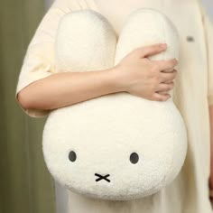 a person holding a white stuffed animal with black eyes on it's face and arms