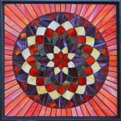 a stained glass window with an orange and purple flower in the center, on top of a black frame