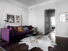 a living room with purple couches and white rugs on the wooden flooring