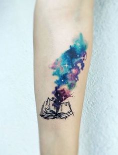 a person with a book tattoo on their arm and the sky is filled with stars